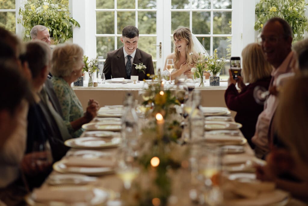 Bride and groom reacting during speeches at wedding breakfast with guests seated at Stockton House in Shropshire
