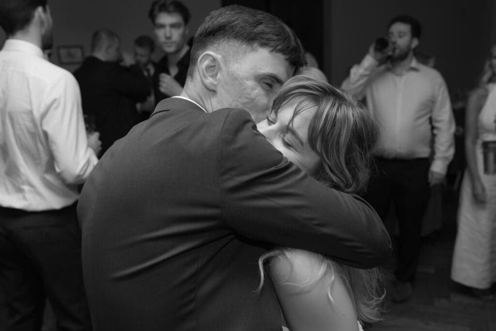 Bride and groom hugging closely during evening wedding reception surrounded by guests