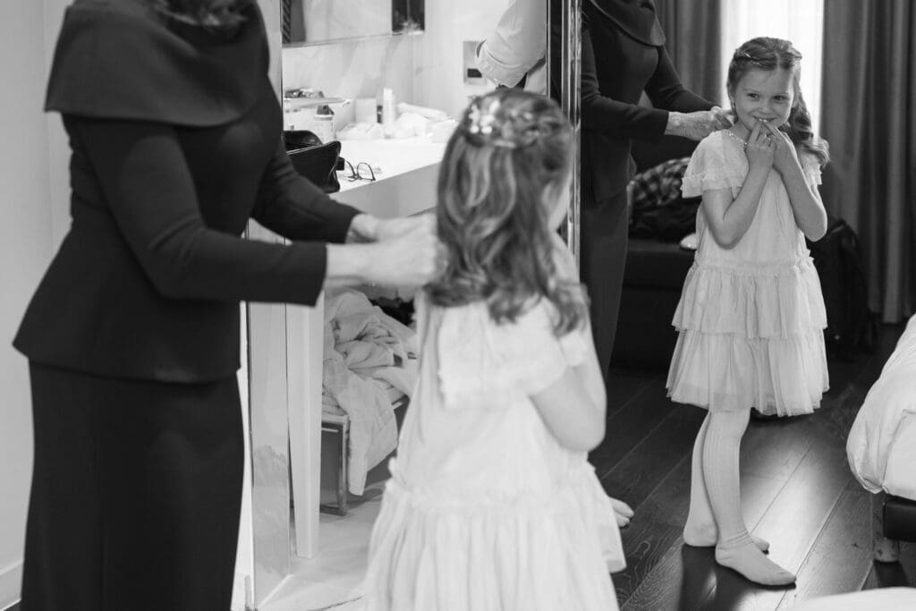 young girl looks at herself in the mirror bashfully as the mother of the bride helps her into her dress
