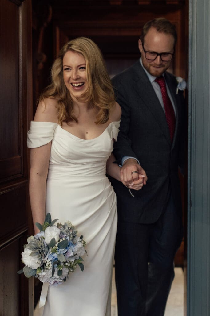 bride and groom arrive at the ceremony, walking through the doors at the Knightsbridge Room in Marylebone Town Hall in London at the start of their wedding