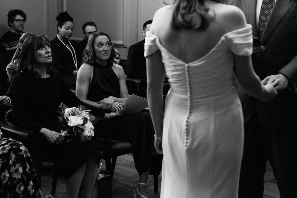 the brides mother and sister look on emotionally while the bride and groom exchange vows during their wedding ceremony at Marylebone Town Hall in London