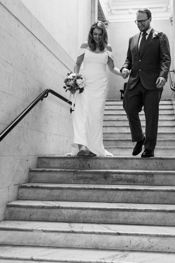 a black and white photo of the bride and groom walking down the iconic interiors of Marylebone Town Hall after their London wedding