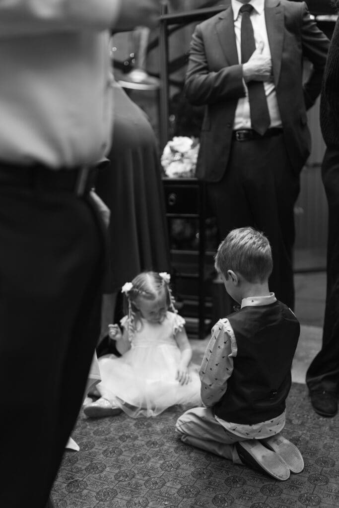 a nephew and his niece playing together on the floor of the greenhouse surrounded by smartly dressed wedding guests