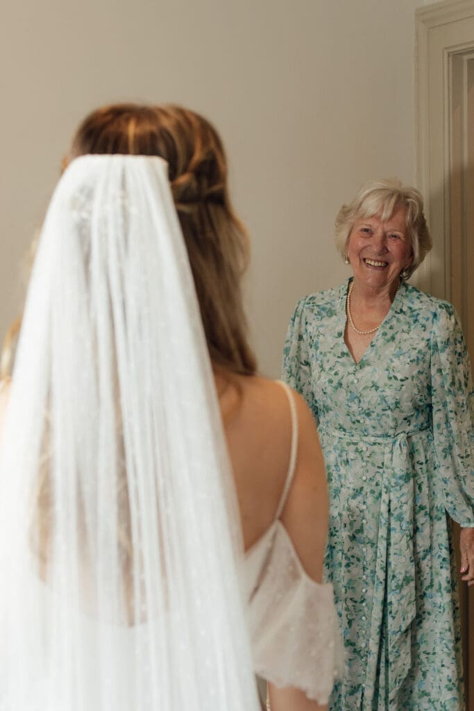 Bride in veil showing her wedding dress to an older family member smiling during morning at Stockton House in Shropshire