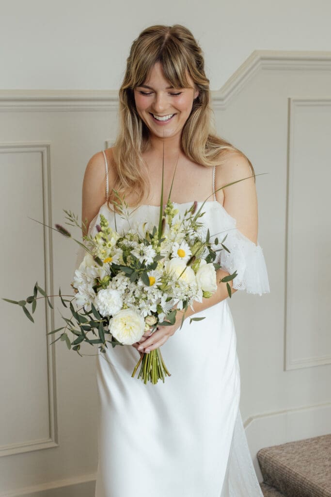 Bride in wedding dress holding bouquet of white flowers and greenery, smiling before ceremony at Stockton House, Shropshire