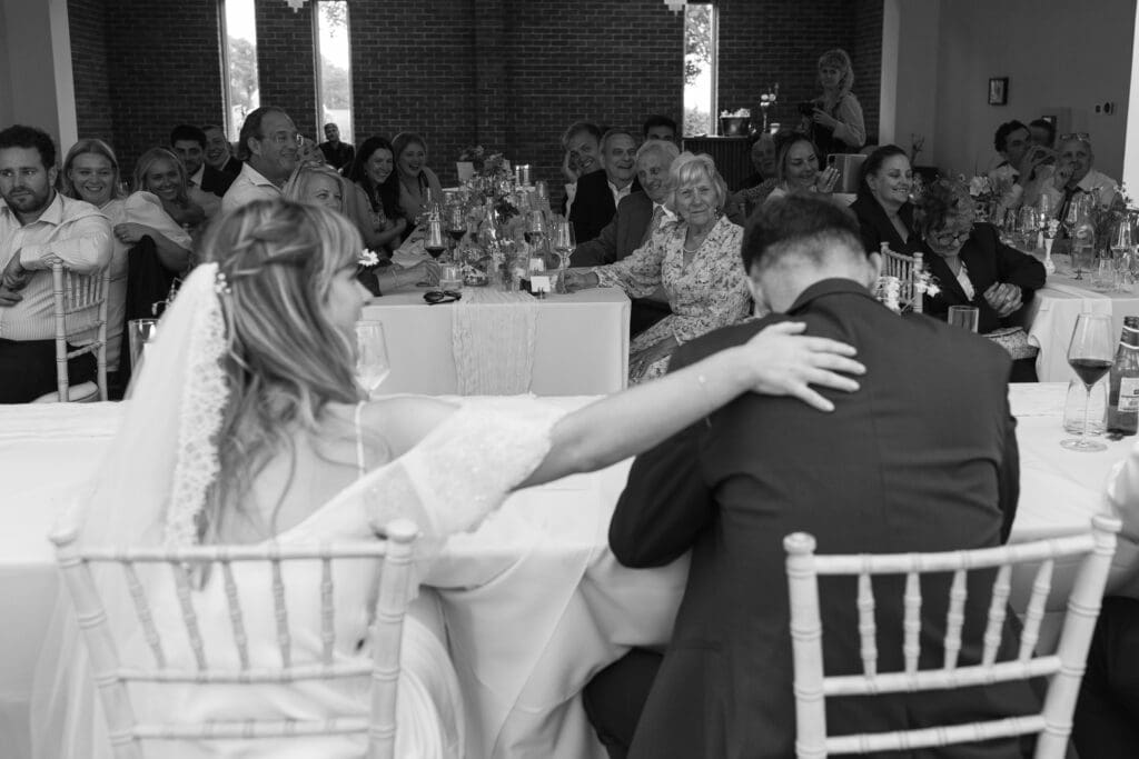 Bride with hand on groom’s back during emotional wedding speech with guests seated around at Stockton House, Shropshire