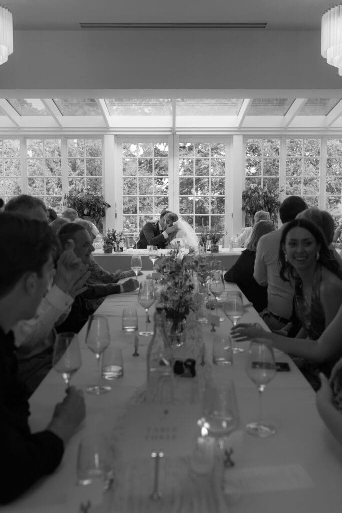 Bride and groom kissing at top table during wedding breakfast while guests sit around them at Stockton House, Shropshire