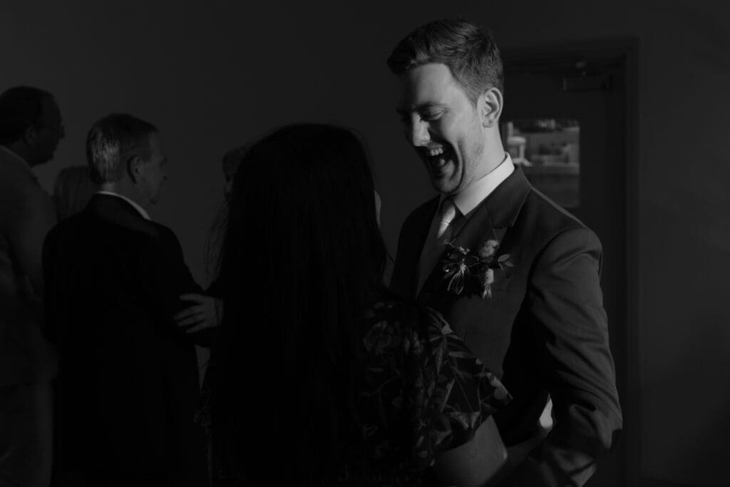 Groom smiling and laughing while greeting a guest during evening wedding reception at Stockton House