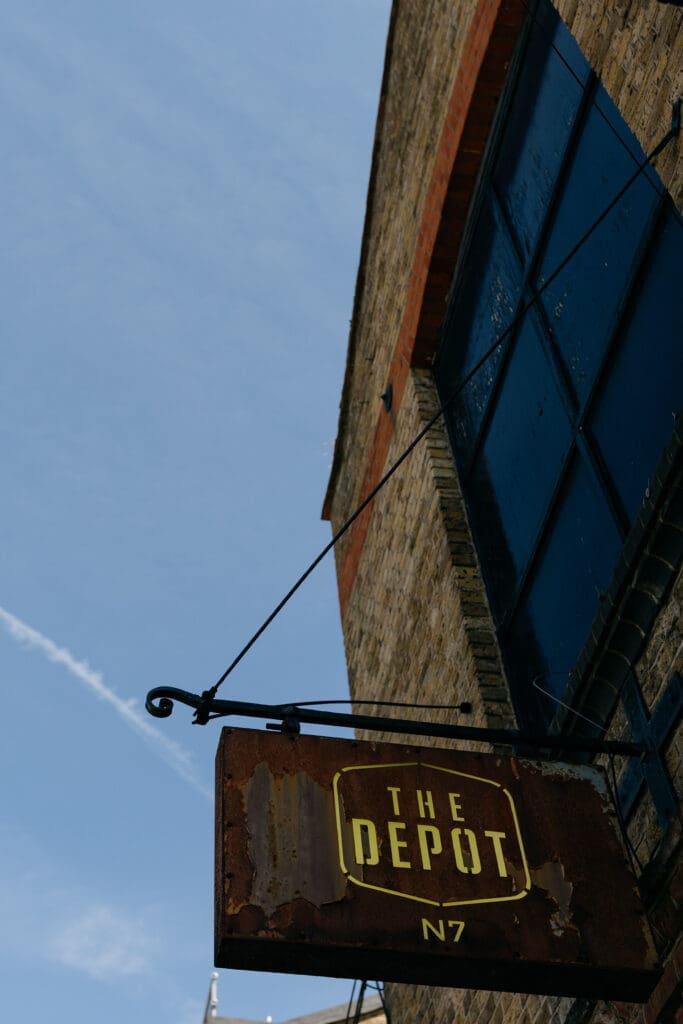 the depot signage hangs mounted on a wall outside The Depot in London in front of a blue sky