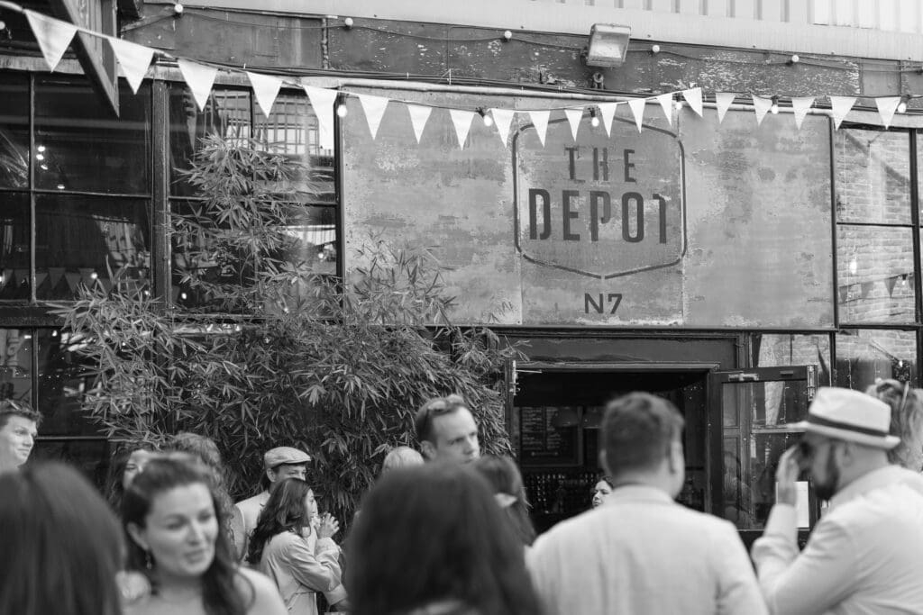 Guests socialising outside The Depot wedding venue beneath bunting and festoon lights.